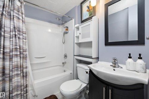 Full bathroom featuring a white tub/shower combination, a dark wood-finish vanity with an integrated sink, a rectangular framed mirror, and a wall-mounted storage cabinet - 1586 Chapman Way, Edmonton, AB - Indoor Photo Showing Bathroom
