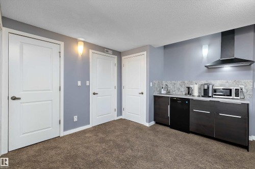 Kitchenette featuring a stainless steel range hood, stone-finish backsplash, and dark wood-finish cabinetry - 1586 Chapman Way, Edmonton, AB - Indoor