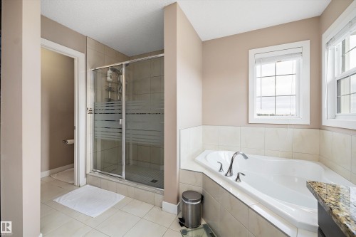 Bathroom featuring a built-in corner soaking tub with deck-mounted chrome fixtures, a separate glass-enclosed shower, and a light-toned tile surround - 1586 Chapman Way, Edmonton, AB - Indoor Photo Showing Bathroom