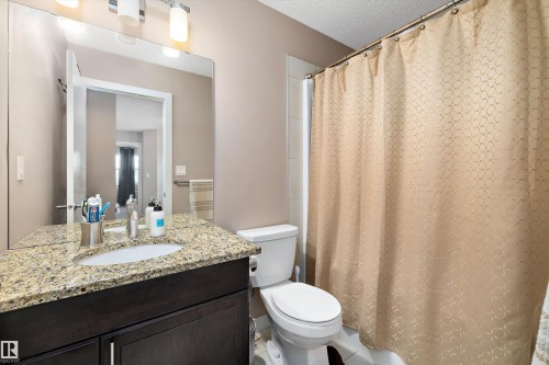 Bathroom featuring a dark wood-finish vanity with a granite-style countertop, an undermount sink, and a large wall-mounted mirror - 1586 Chapman Way, Edmonton, AB - Indoor Photo Showing Bathroom