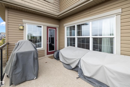 Private outdoor patio featuring a red-framed glass-paneled door, large grid-pattern windows, and tan horizontal siding - 1586 Chapman Way, Edmonton, AB - Outdoor With Exterior