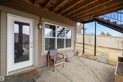 Covered concrete patio area with a white glass-paneled door, exterior wall lantern, and a multi-pane window - 1586 Chapman Way, Edmonton, AB - Outdoor With Deck Patio Veranda With Exterior