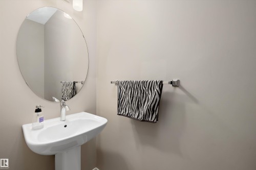 Pedestal sink with chrome faucet, complemented by a large oval wall mirror and contemporary wall lighting - 1586 Chapman Way, Edmonton, AB - Indoor Photo Showing Bathroom