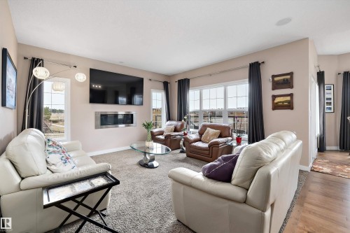 Spacious living area featuring neutral-toned walls, plush carpet flooring, a wall-mounted fireplace, and multiple large windows - 1586 Chapman Way, Edmonton, AB - Indoor Photo Showing Living Room With Fireplace