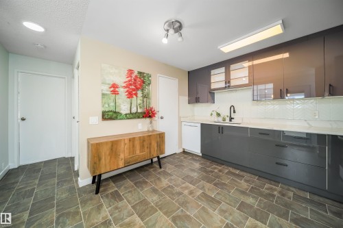 Modern kitchen featuring dark gray cabinetry, white countertops, a white herringbone tile backsplash, and dark tile flooring - 5303 21 Avenue, Edmonton, AB - Indoor Photo Showing Kitchen