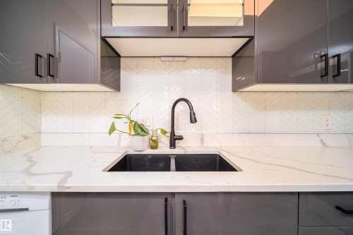 Contemporary kitchen featuring a dual-basin sink with a matte black gooseneck faucet, white stone countertop with natural veining, and a white geometric tile backsplash - 5303 21 Avenue, Edmonton, AB - Indoor Photo Showing Kitchen With Double Sink