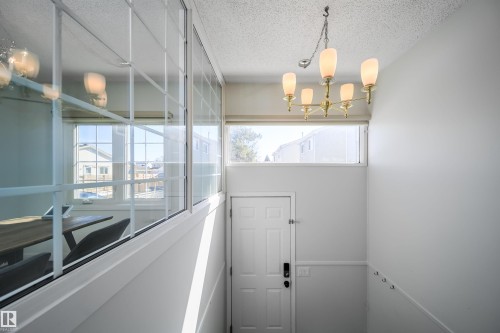 Upper-level landing featuring a brass chandelier with frosted glass shades, a transom window, and a built-in wall of windows with grid patterns - 5303 21 Avenue, Edmonton, AB - Indoor Photo Showing Other Room