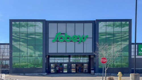 Modern commercial facade featuring extensive glass panels with green-tinted reflections - 5303 21 Avenue, Edmonton, AB - 