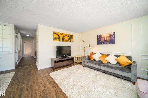 Living area featuring wood-finish flooring, decorative wall molding, and a wall-mounted sconce - 5303 21 Avenue, Edmonton, AB - Indoor Photo Showing Living Room