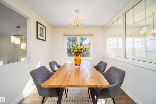 Dining area featuring wood-finish flooring, a contemporary chandelier, and a large window providing ample illumination - 5303 21 Avenue, Edmonton, AB - Indoor Photo Showing Dining Room