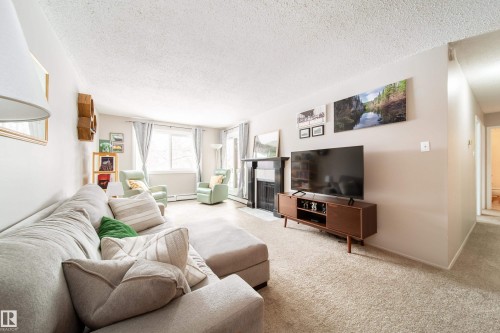 Spacious living area featuring neutral carpeting, a black fireplace surround, and multiple windows - 220 14819 51 Avenue, Edmonton, AB - Indoor Photo Showing Living Room