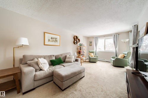 Carpeted living area featuring white walls and a large window - 220 14819 51 Avenue, Edmonton, AB - Indoor Photo Showing Living Room