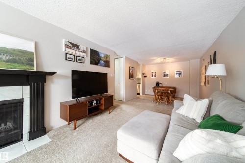 Living area featuring a fireplace with a black mantel and white tile surround - 220 14819 51 Avenue, Edmonton, AB - Indoor Photo Showing Living Room With Fireplace