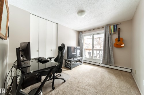 Spacious room featuring neutral carpeting, a full-height closet with bi-fold doors, a sliding glass door providing natural light, and a baseboard heating system - 220 14819 51 Avenue, Edmonton, AB - Indoor Photo Showing Office