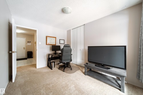 Carpeted room featuring a double-door closet, a ceiling-mounted light fixture, and a doorway opening to a tiled entrance area - 220 14819 51 Avenue, Edmonton, AB - Indoor