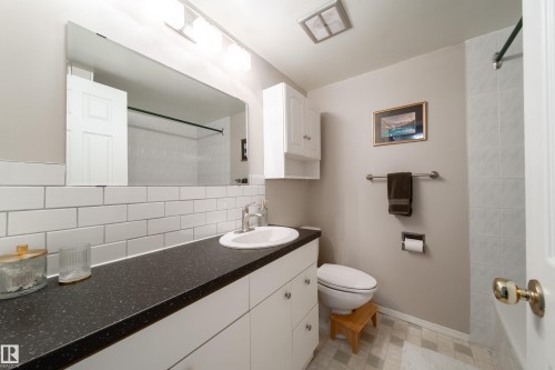 Bathroom featuring a white subway tile backsplash, a dark speckled countertop, and white cabinetry - 220 14819 51 Avenue, Edmonton, AB - Indoor Photo Showing Bathroom