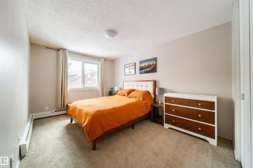 Carpeted bedroom featuring a large window, neutral wall paint, and a textured ceiling - 220 14819 51 Avenue, Edmonton, AB - Indoor Photo Showing Bedroom