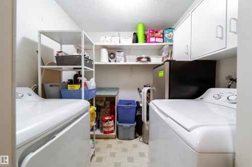 Dedicated laundry area featuring a washer and dryer, integrated shelving, and white overhead cabinetry - 220 14819 51 Avenue, Edmonton, AB - Indoor Photo Showing Laundry Room