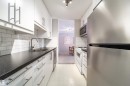 Galley kitchen featuring white cabinetry with brushed nickel hardware, dark speckled countertops, subway tile backsplash, and stainless steel appliances - 220 14819 51 Avenue, Edmonton, AB  - Indoor Photo Showing Kitchen With Double Sink 