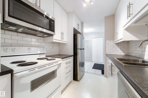 Galley kitchen featuring white cabinetry, dark speckled countertops, and a white subway tile backsplash - 220 14819 51 Avenue, Edmonton, AB - Indoor Photo Showing Kitchen With Double Sink