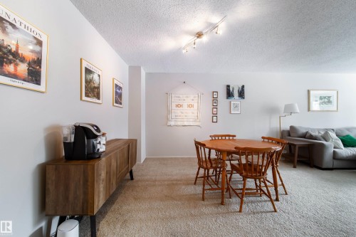 Open-concept living area featuring light-toned carpeting, track lighting, and a textured ceiling - 220 14819 51 Avenue, Edmonton, AB - Indoor