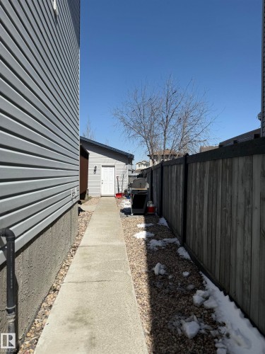 Side yard featuring a concrete pathway, gravel landscaping, and a wooden privacy fence - 73 Birchmont Drive, Leduc, AB - Outdoor