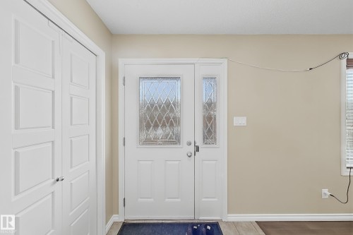 Entryway featuring a decorative glass main door with a sidelight, neutral wall paint, white baseboards, and a bi-fold closet - 3609 Weidle Bend Bend, Edmonton, AB - Indoor Photo Showing Other Room