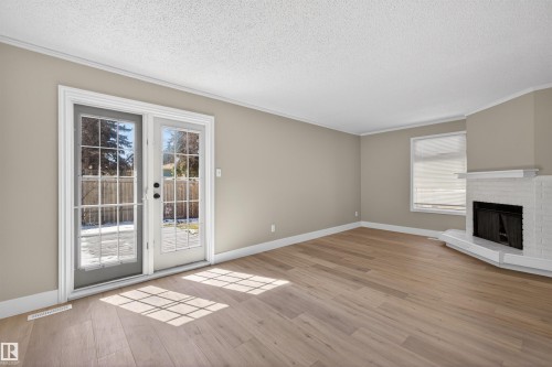 Bright living area featuring wood-finish flooring, neutral-toned walls, and white crown molding - 11 Greenfield Estates, St. Albert, AB - Indoor With Fireplace