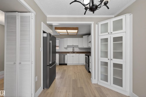 Kitchen entryway featuring wood-finish flooring, white built-in cabinetry with reeded glass doors, and a dark stainless steel refrigerator - 11 Greenfield Estates, St. Albert, AB - Indoor Photo Showing Kitchen