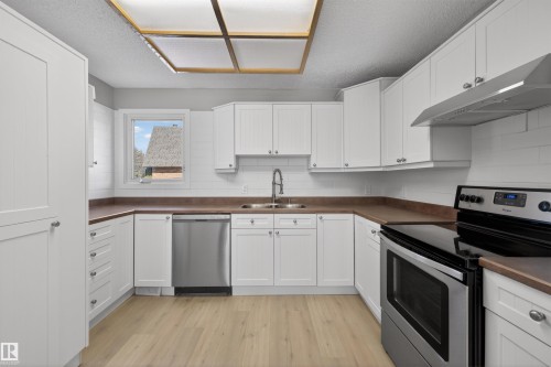 Kitchen featuring white shaker-style cabinetry, wood-finish flooring, a stainless steel dishwasher, a range oven, and a white subway tile backsplash - 11 Greenfield Estates, St. Albert, AB - Indoor Photo Showing Kitchen With Double Sink