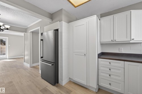 Kitchen featuring white shaker-style cabinetry with dark countertops, a stainless steel refrigerator, and wood-finish flooring - 11 Greenfield Estates, St. Albert, AB - Indoor