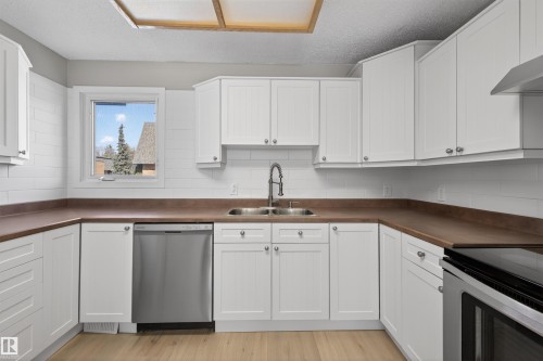 Kitchen featuring white shaker-style cabinetry, wood-finish countertops, stainless steel appliances, a double basin sink with a gooseneck faucet, and light wood-finish flooring - 11 Greenfield Estates, St. Albert, AB - Indoor Photo Showing Kitchen With Double Sink