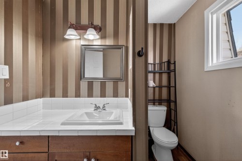 Bathroom vanity featuring a white tile countertop, integrated sink, and wood-finish cabinetry - 11 Greenfield Estates, St. Albert, AB - Indoor Photo Showing Bathroom