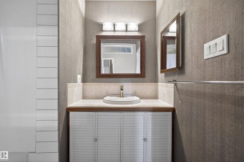 Bathroom vanity featuring a tile countertop, integrated sink, and louvered cabinetry - 11 Greenfield Estates, St. Albert, AB - Indoor Photo Showing Bathroom