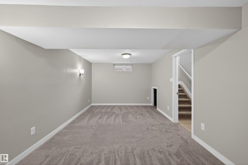 Spacious lower-level room featuring light gray walls, plush gray patterned carpeting, recessed ceiling lighting, and modern sconce fixtures - 11 Greenfield Estates, St. Albert, AB - Indoor Photo Showing Other Room