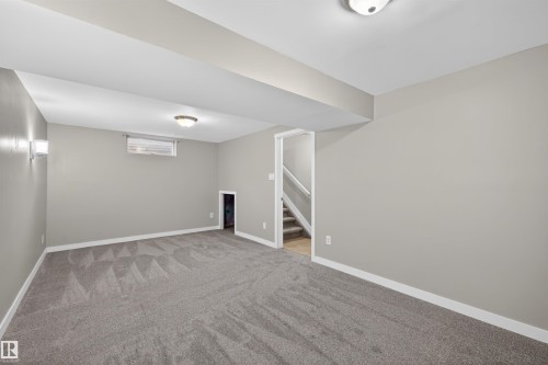 Spacious carpeted room featuring a recessed window, a built-in storage nook, and a staircase with white railings - 11 Greenfield Estates, St. Albert, AB - Indoor
