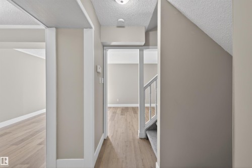 Hallway featuring wood-finish flooring, light grey painted walls, white trim, and a carpeted staircase with white balusters - 11 Greenfield Estates, St. Albert, AB - Indoor