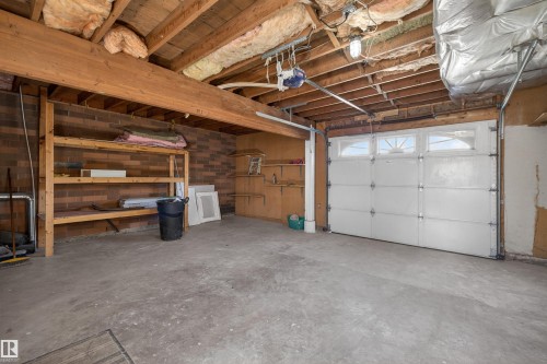 Garage space featuring a concrete floor, exposed wood beam ceiling, and brick wall accents - 11 Greenfield Estates, St. Albert, AB - Indoor Photo Showing Garage