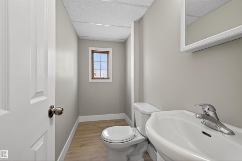 Compact bathroom featuring wood-finish flooring, a white pedestal sink with a chrome faucet, and a toilet - 11 Greenfield Estates, St. Albert, AB - Indoor Photo Showing Bathroom