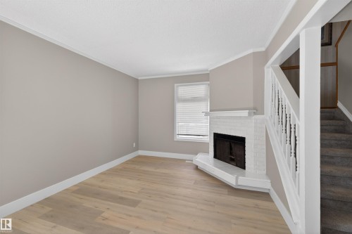 Living area featuring wood-finish flooring, a white brick fireplace, and neutral wall paint - 11 Greenfield Estates, St. Albert, AB - Indoor Photo Showing Other Room With Fireplace