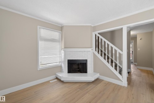 Corner fireplace with white painted brick surround and hearth, light wood-finish flooring, staircase with white railings, neutral wall color, and white trim - 11 Greenfield Estates, St. Albert, AB - Indoor With Fireplace