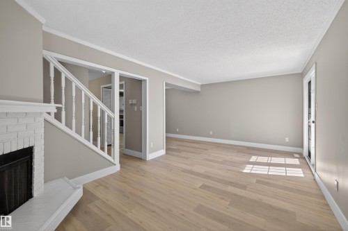 Spacious living area featuring light wood-finish flooring, a white brick fireplace, white crown molding, and neutral wall tones - 11 Greenfield Estates, St. Albert, AB - Indoor With Fireplace