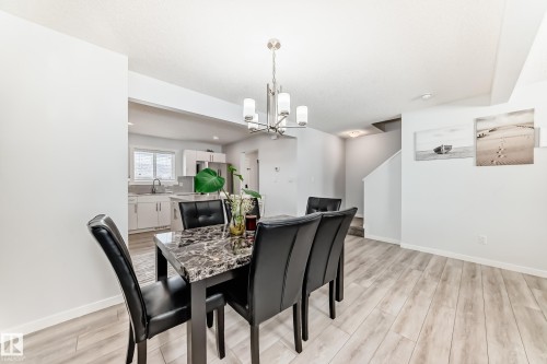 Dining area featuring wood-finish flooring, a contemporary chandelier, and a partial view of the kitchen with white cabinetry - 2505 14 Avenue, Edmonton, AB - Indoor Photo Showing Dining Room