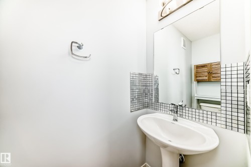 Pedestal sink with chrome faucet, framed by a large mirror and mosaic tile accents - 2505 14 Avenue, Edmonton, AB - Indoor Photo Showing Bathroom