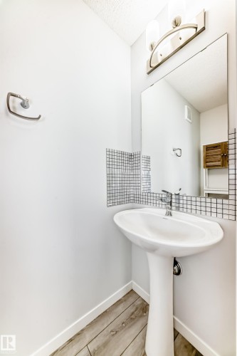 Pedestal sink with chrome faucet, glass mosaic tile backsplash, rectangular mirror, and a wall-mounted light fixture - 2505 14 Avenue, Edmonton, AB - Indoor Photo Showing Bathroom