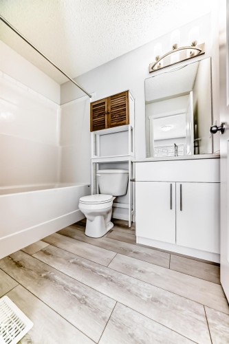 Wood-finish flooring throughout the bathroom featuring a white vanity with integrated sink, modern hardware, and an overhead vanity light - 2505 14 Avenue, Edmonton, AB - Indoor Photo Showing Bathroom