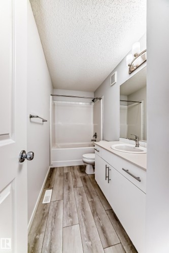 Bathroom featuring wood-finish flooring, a white vanity with a light-toned countertop, a shower-tub combination, and a mirror with overhead lighting - 2505 14 Avenue, Edmonton, AB - Indoor Photo Showing Bathroom