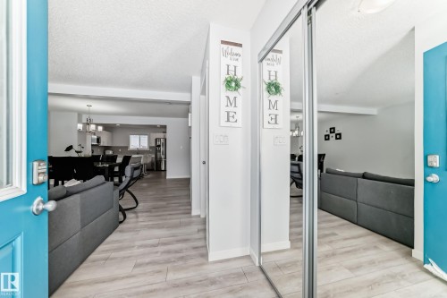 Entryway featuring a bright blue door with frosted glass, wood-finish flooring, a mirrored closet, and a clear line of sight into the kitchen and dining areas - 2505 14 Avenue, Edmonton, AB - Indoor Photo Showing Other Room