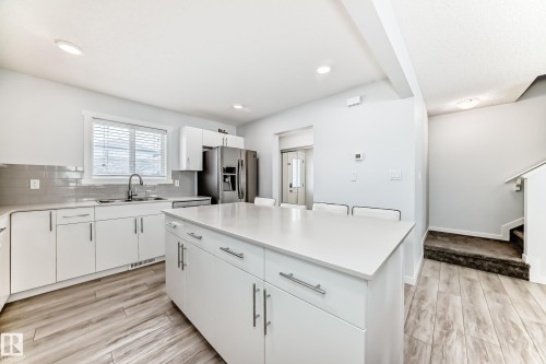 Kitchen featuring a large central island with seating, white cabinetry, integrated stainless steel appliances, a grey subway tile backsplash, and wood-finish flooring - 2505 14 Avenue, Edmonton, AB - Indoor Photo Showing Kitchen