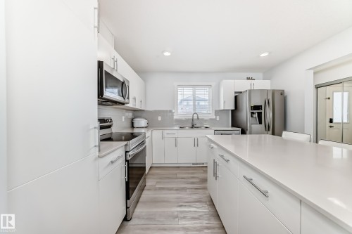 Modern kitchen featuring white cabinetry, light-toned countertops, stainless steel appliances, a center island, and wood-finish flooring - 2505 14 Avenue, Edmonton, AB - Indoor Photo Showing Kitchen With Upgraded Kitchen